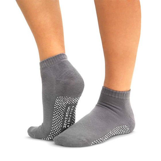 A person wearing gray non-slip yoga socks. Showing the bottom part of the yoga socks with white PVC dots.